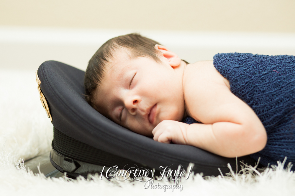 newborn photographer photographing a newborn laying his head on a police officer's cap 