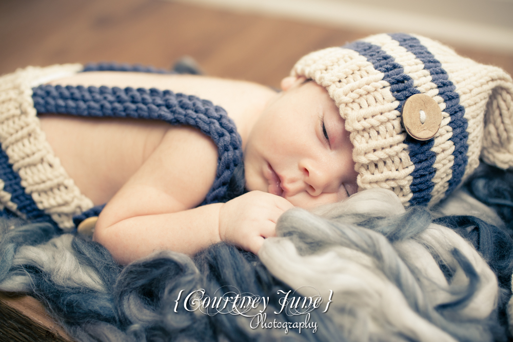 newborn photographer photographing a newborn in a knit jumper laying on stomach with one eye open 