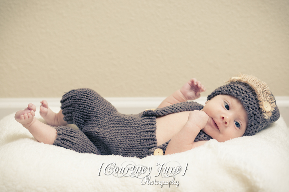 newborn photographer photographing a newborn in a brown knit jumper laying on his back smiling