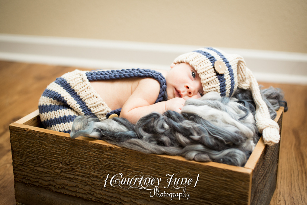 newborn photographer photographing a newborn in knit outfit and hat in a wooden crate